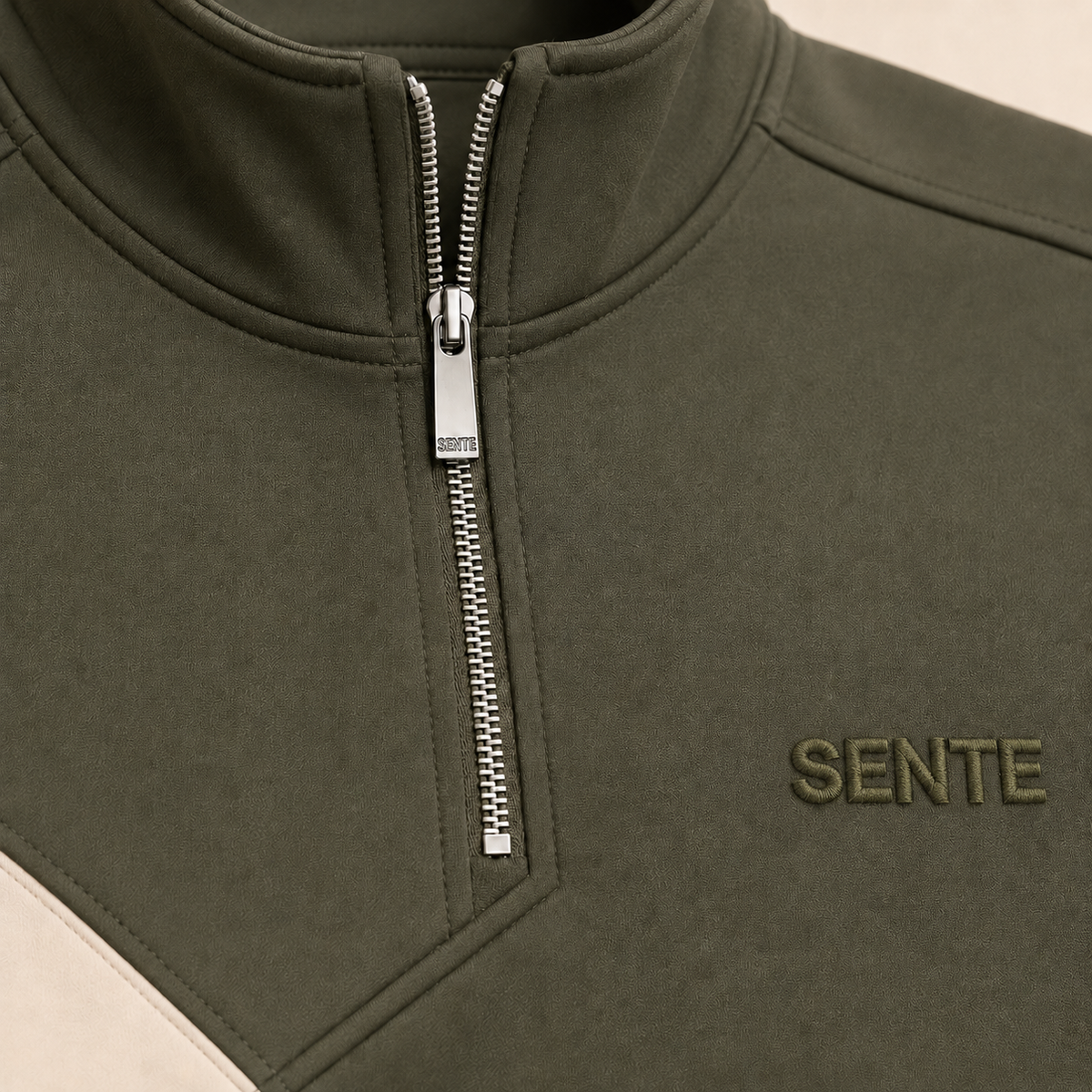 Close-up of a dark olive green quarter-zip pullover with a silver zipper and the brand name 'SENTE' embroidered on the chest.