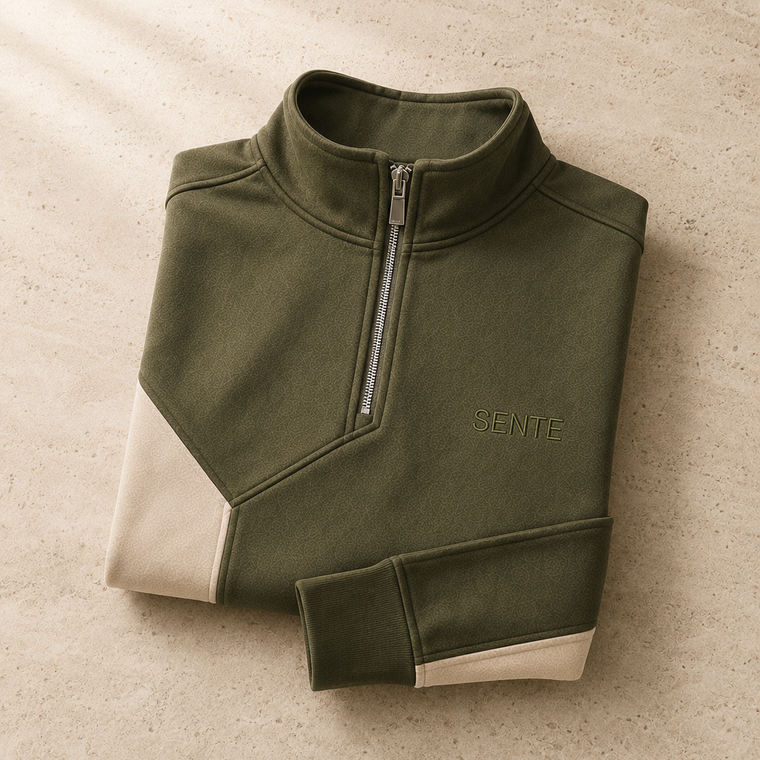 An olive green quarter-zip pullover sweatshirt with cream color-blocked panels on the lower front and cuffs, featuring the brand name 'SENTE' embroidered on the chest, laid flat on a textured beige surface.
