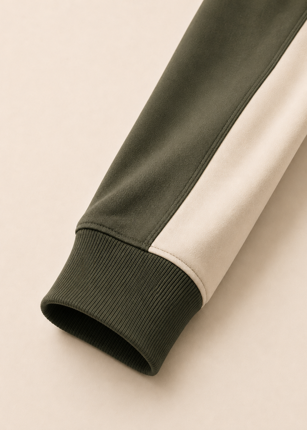 Close-up of a color-blocked sweatshirt sleeve with an olive green ribbed cuff and a vertical off-white stripe on a light beige background.