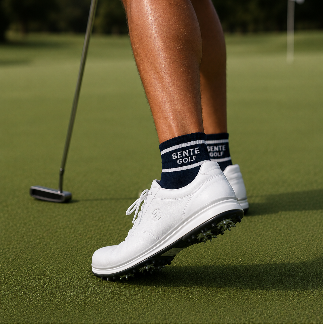 Person on a golf course wearing white shoes and navy socks with 'Sente Golf' branding.